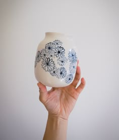 a hand holding up a white and blue vase with flowers on it's side