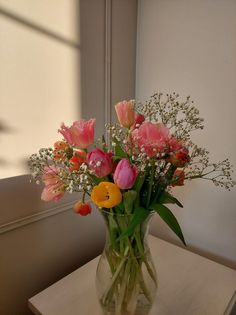 a vase filled with lots of flowers sitting on top of a table next to a window