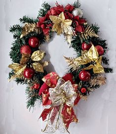 a red and gold christmas wreath hanging on a white wall with ornaments around the wreath