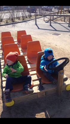 two young boys sitting on seats in the sand