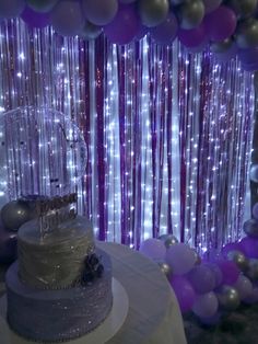 a white cake sitting on top of a table next to purple and silver balloons in the background