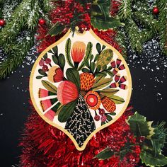 a christmas ornament hanging from a tree with red tinsel and green leaves