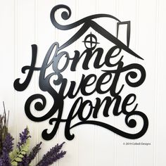 a metal sign that says home sweet home with a house on it next to some purple flowers