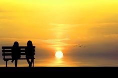 two people sitting on a bench watching the sun set over the ocean royalty photo - illustration