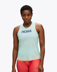 a woman is posing for the camera in her sports bra and tights, wearing an aqua tank top that says hoka