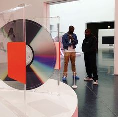 two men standing next to each other in front of a glass case with a cd on it