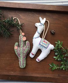 two stuffed llamas are on a wooden table next to a cactus and pineconi