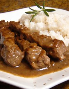 a white plate topped with meat and gravy covered in gravy next to rice