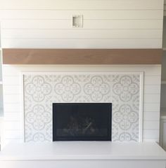 a white fireplace with a wood mantle in the middle and a tile design on it