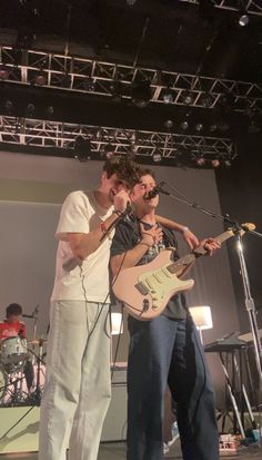 two men standing on stage with guitars and microphones