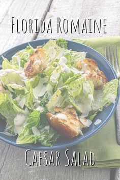 a blue bowl filled with salad on top of a wooden table next to a fork