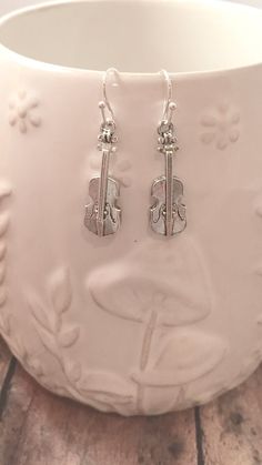 a pair of silver earrings sitting on top of a white bowl in front of a wooden floor