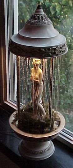 a statue in a glass case on a window sill next to a lamp with chains hanging from it