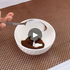 a person is spooning chocolate into a white bowl with a spoon in it on a brown mat