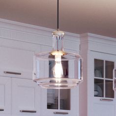 a clear glass light fixture hanging from the ceiling in a kitchen with white cabinets and cupboards