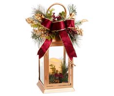 a lighted lantern with a red bow and pine cones on it's top, decorated with evergreens and berries