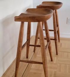 three wooden stools sitting on top of a hard wood floor next to a wall