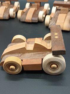 wooden toy cars are lined up on a black table top with other wood toys in the background