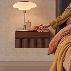 a woman sitting in bed next to a table with a lamp on top of it