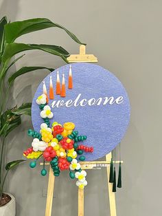 a welcome sign made out of balloons on a easel next to a potted plant