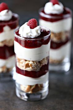 three desserts with raspberries and whipped cream on top are sitting in small glasses