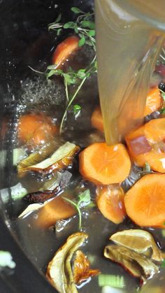 carrots and other vegetables are being cooked in a pot with liquid pouring over them