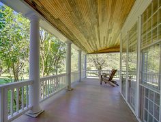 an empty porch with rocking chairs on the side and trees in the backgroud