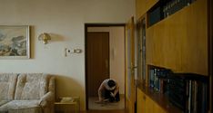 a man kneeling down in front of a couch next to a book shelf filled with books