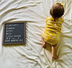 a baby laying on top of a bed next to a sign