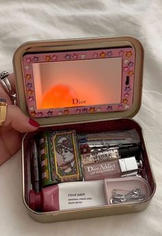 a woman's hand is holding an open tin box with various items inside