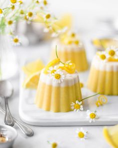 small cakes with yellow and white frosting are on a plate next to silver utensils