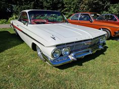 two old cars parked next to each other in the grass