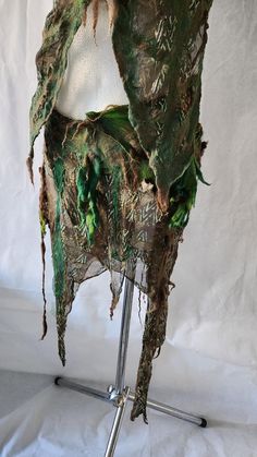 a chair covered in green leaves on a metal stand with white cloth draped over it