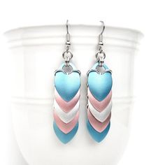 "Lightweight anodized aluminum scales cascade over one another in these stunning transgender pride chainmail earrings. There is one scale of each color of the 5 stripe flag: light blue, light pink, white, light pink, and light blue. The gorgeous scales have a subtle shimmer and are anodized on both sides as well as the edges. Silver aluminum jump rings link the scales.  Including the French hook ear wire, the earrings measure 2-3/4\" in length. They are just over 1/2\" wide. Dimes shown for scale. The current ear wires are hypoallergenic surgical stainless steel French hooks, but can be changed to steel lever backs if you prefer. Please select your ear wire preference from the drop down menu. See more trans jewelry here: https://www.etsy.com/shop/TattooedAndChained?search_query=transgender Chainmail Earrings, Trans Pride Flag, Chain Maille Jewelry, White Jewelry Box, Trans Pride, Hard Metal, Chain Mail, White Jewelry, Pride Flag