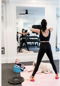 a woman is doing yoga with her baby and dog in front of the gym mirror