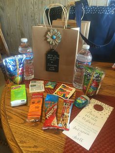 an assortment of candy and snacks on a table with a bag, water bottle, and note card