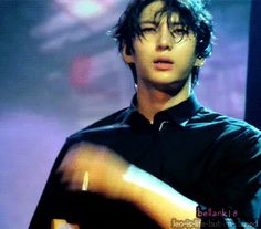 a young man with glasses is playing an acoustic guitar in front of a purple background