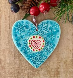 a blue heart shaped ornament sitting on top of a wooden table next to berries and pine cones