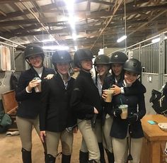 four women in riding gear are posing for a photo while holding drinks and smiling at the camera