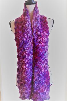 I hand knit this scarf with a combination of two different yarns.   The color change yarn (cranberry, blue, and white), is 100 % soft acrylic.  The other yarn is a solid cranberry color, and is 30% mohair (for a touch of fuzzy luxury), 30% nylon (for durability), and 40% acrylic (for softness).  The scarf is knitted in a wavy pattern.  It is 63 inches long, and 6 inches wide. MaudieRose is my wonderful chocolate labradoodle.  She is a rescue from a puppy mill, and is slowly learning how to be a dog.  Maudie knows too well how it feels to be cold; she is my inspiration for making these warm and cozy scarves. Ours is a non-smoking home. Purple Yarn Scarf, Hand Knitted Purple Knitting Pattern, Purple Crochet Scarf One Size, Purple Crochet Scarves One Size, One Size Purple Crochet Scarf, Hand Knitted Yarn Scarves, Purple Crochet Yarn Scarves, Purple Knitted Winter Scarves, Handmade One Size Acrylic Knitting Pattern