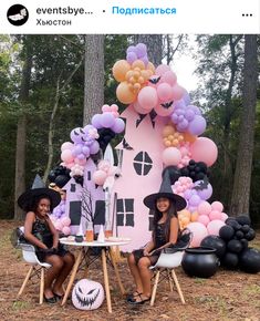 two women sitting at a table in front of a pink house with balloons and decorations