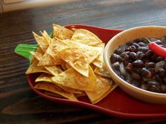 a bowl of black beans and tortilla chips on a red plate with a chili pepper