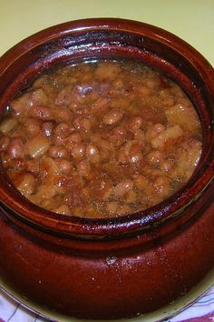 a wooden bowl filled with beans on top of a table next to a white plate