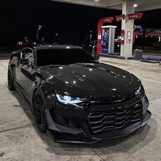 a black chevrolet camaro is parked in front of a gas station at night time