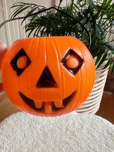 a carved pumpkin with eyes and mouth on a table next to a potted plant