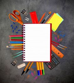 an open notebook surrounded by school supplies such as pens, pencils, scissors and markers