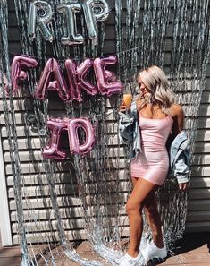 a woman in a pink dress standing next to a wall with balloons and the words fake do