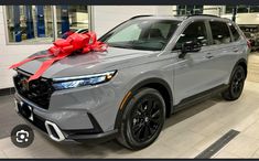 a gray car with a red bow on it's hood in a showroom