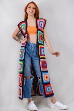 a woman wearing a colorful crochet cardigan and jeans, standing in front of a white background