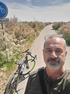 a man standing in front of a bike on the side of a road next to a sign